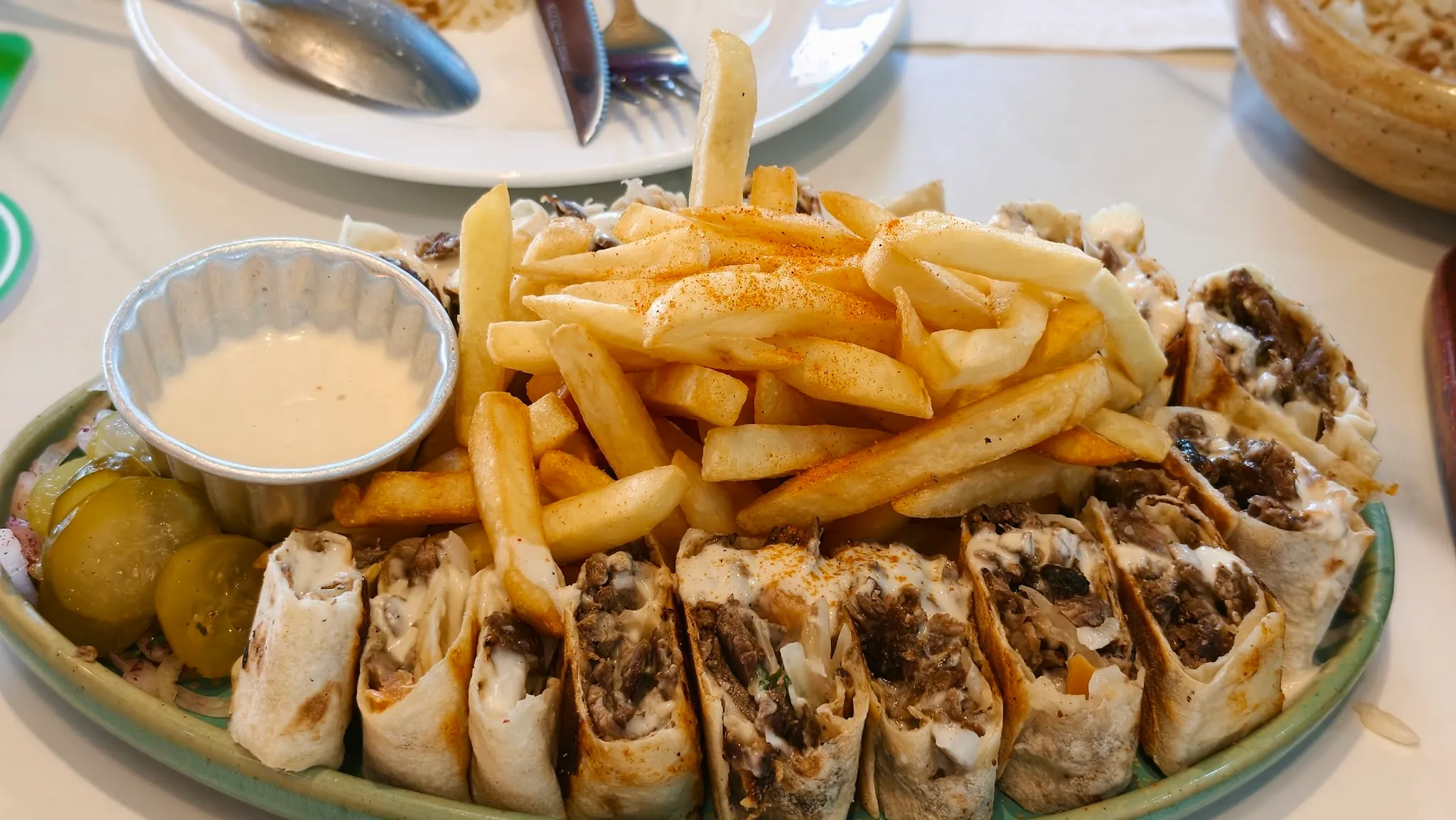 Sliced meat shawarma rolls with fries, pickles and tahini sauce