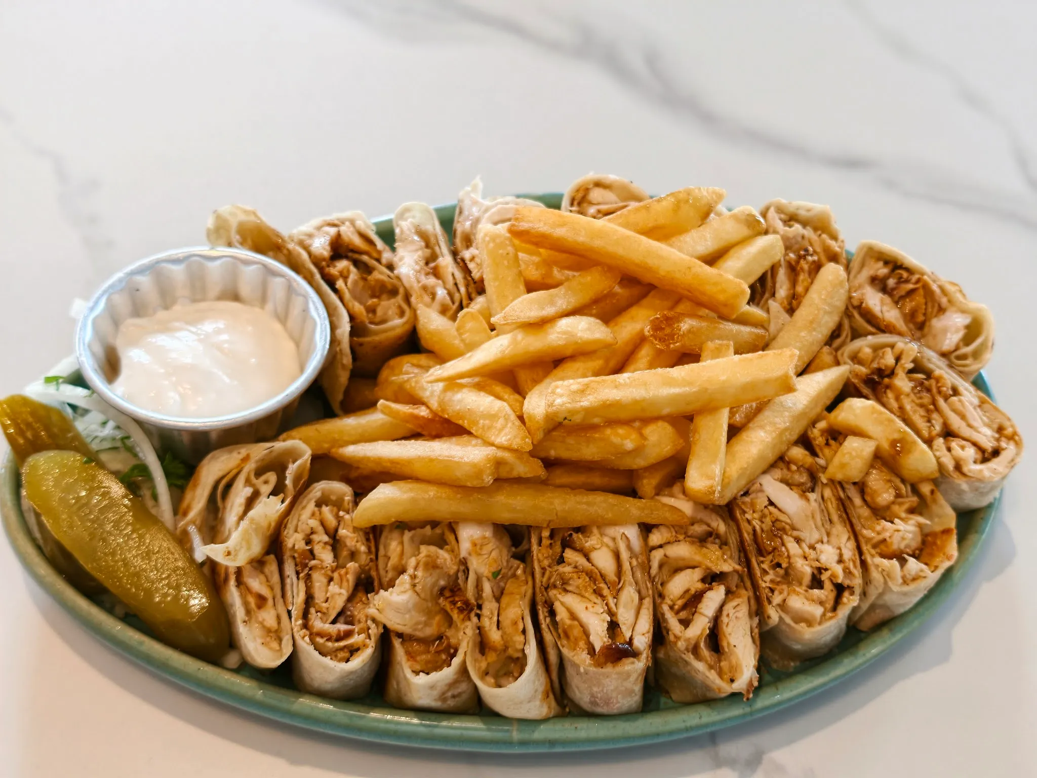 Chicken shawarma rolls sliced and piled with fries, garlic sauce and pickles