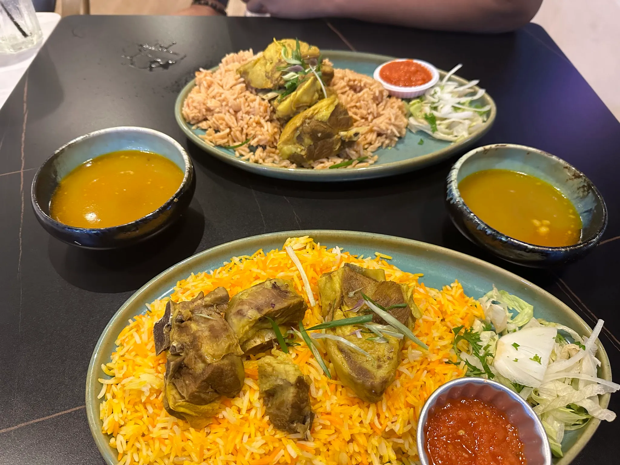 Lamb on spiced mandi-style rice with bowls of broth and tomato-chilli relish