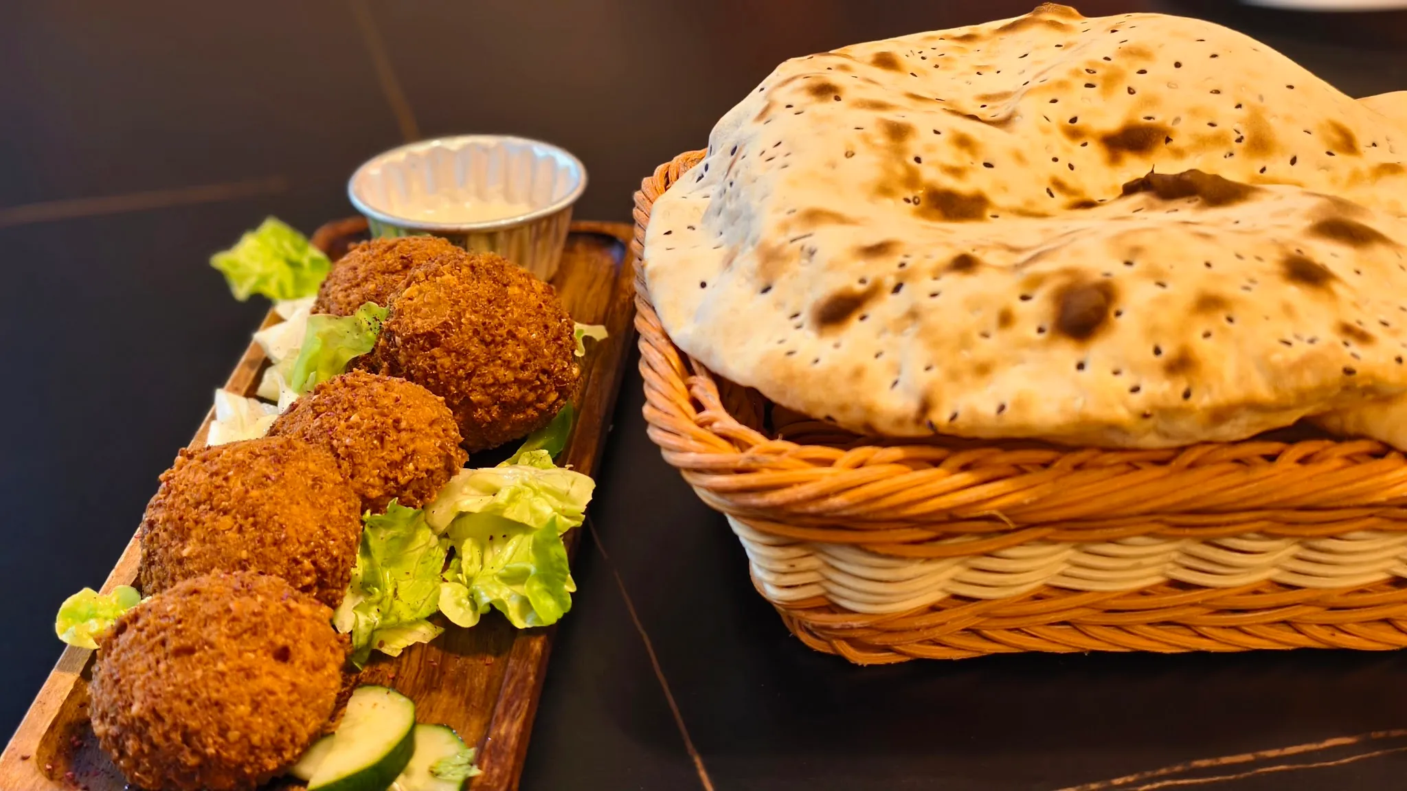 Crisp falafel on salad leaves with cucumber and tahini dip, beside a basket of fresh flatbread